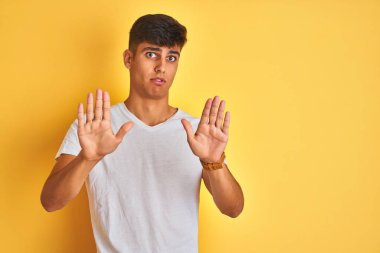 İzole edilmiş sarı arka plan üzerinde duran beyaz tişörtlü genç Hintli adam avuç içlerini hareket ettiriyor. Korkmuş ve iğrenç bir ifadeyle reddediyor. Dur ve yasakla.