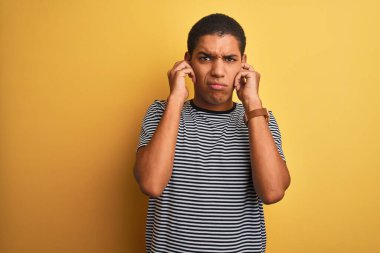 Genç yakışıklı Arap adam izole edilmiş sarı arka planda donanma tişörtü giyiyor. Yüksek sesli müzik sesi için kulakları parmaklarıyla kapatıyor. Sağır kavramı.