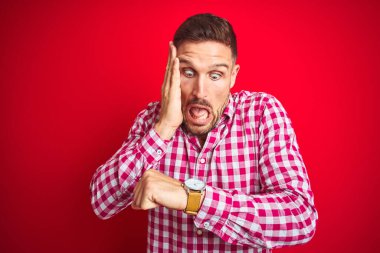 Genç ve yakışıklı bir adam, kırmızı izole edilmiş arka planda. Saatine bakıyor, endişeli, geç kalmaktan korkuyor.