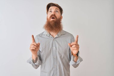 İzole edilmiş beyaz arka plan üzerinde duran genç, kızıl saçlı ve İrlandalı adam şaşırmış ve şaşırmıştı. Parmaklarıyla işaret ediyor ve kollarını kaldırıyordu..