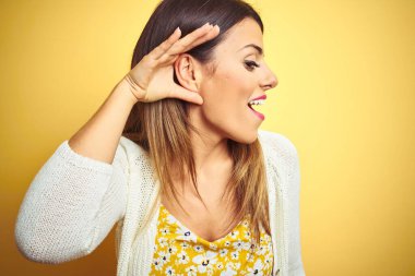 Sarı arka plan üzerinde duran ceketli genç ve güzel bir kadın. Kulağından kulağa gülümsüyor. Dedikodulara ve dedikodulara kulak veriyor. Sağırlık kavramı.