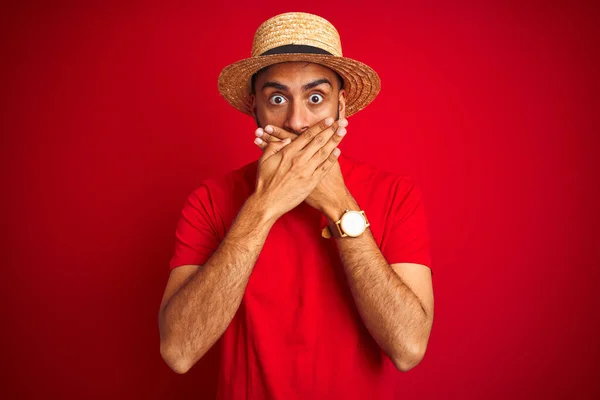 Tシャツを着た若いハンサムなインド人男性と 孤立した赤い背景の上の帽子は 間違いのために手で口を覆いショックを受けました 秘密概念 — ストック写真