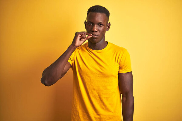 Young african american man wearing casual t-shirt standing over isolated yellow background mouth and lips shut as zip with fingers. Secret and silent, taboo talking