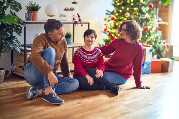 Beautiful family smiling happy and confident. Sitting on the floor with smile on face around christmas tree and gifts at home