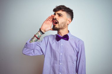 Mor gömlekli ve papyonlu genç adam izole edilmiş beyaz arka planda avazı çıktığı kadar bağırıyor ve avazı çıktığı kadar bağırıyordu. İletişim konsepti.