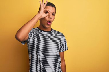 İzole edilmiş sarı arka planda donanma tişörtü giyen yakışıklı Arap adam şaşırmış yüz ifadesiyle şaşırmış ve parmaklarından bakan bir hareket yapıyor. İnançsız ifade.
