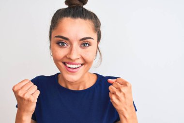 Mavi günlük tişört giyen genç güzel bir kadın izole edilmiş beyaz arka planda durup gururla bağırıyor ve zaferi ve başarıyı kutluyor. Çok heyecanlı, coşkulu bir duygu.