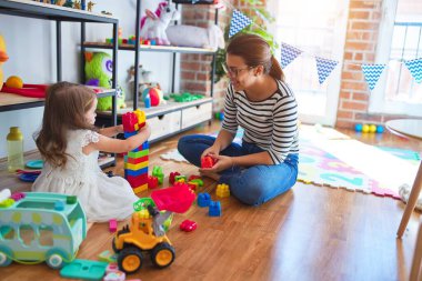 Güzel öğretmen kadın ve bebek anaokulunda bir sürü oyuncağın etrafında taşlarla oynuyorlar.