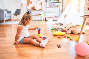 Genç güzel sarışın kız anaokulunda oyuncaklarla eğleniyor, gülümseyerek evde bütünleşme oyuncaklarıyla oynuyor.