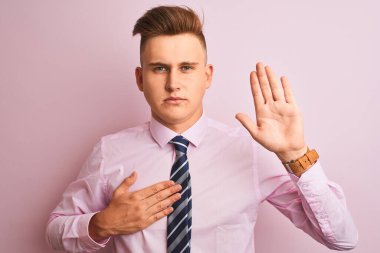 Gömlek ve kravat takan genç yakışıklı bir işadamı pembe arka planda dikilip avuçlarında ve göğsünde yemin ederek sadakat yemini ediyor.