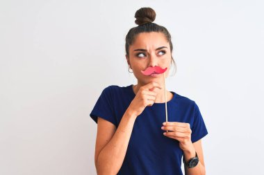 Genç, güzel bir kadın, izole edilmiş beyaz arka plan üzerinde parti bıyığı tutuyor. Ciddi bir yüz. Soru sormayı düşünüyor.