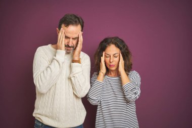 Güzel bir orta yaşlı çift, izole edilmiş mor arka plan üzerine kışlık kazak giyiyorlar ve stres yüzünden başları ağrıyordu. Migren ağrısı..