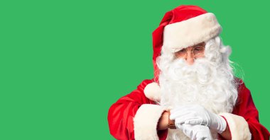 Orta yaşlı yakışıklı adam, Noel Baba kostümü ve sakal takmış, saati kontrol ediyor, rahat ve kendinden emin.