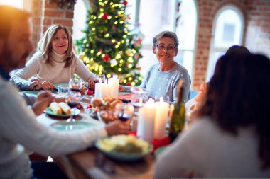 Aile ve arkadaşlar Noel arifesini geleneksel yemek ve dekorasyonla birlikte evde yemek yiyorlar. Hep birlikte masaya oturuyorlar.
