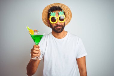 Yazın komik giyinen Hintli adam izole edilmiş beyaz arka planda kokteyl içerken kendine güveni tam bir yüz ifadesiyle ciddi düşünüyor.