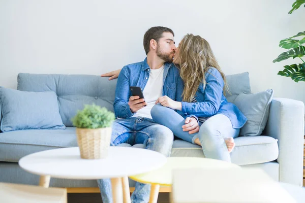 Junges verliebtes Paar umarmt sich auf dem Sofa sitzend mit Smartphone — Stockfoto