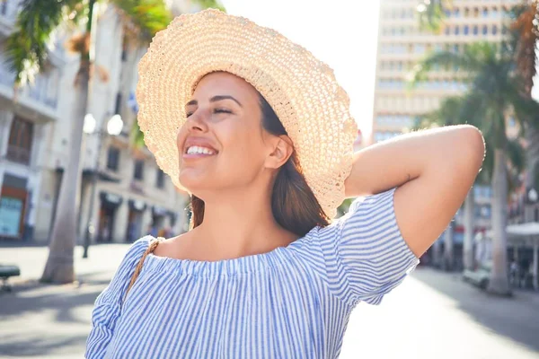 Genç ve güzel bir kadın mutlu bir şekilde gülümsüyor güneşli bir yaz gününde şehir sokaklarında yürüyor.