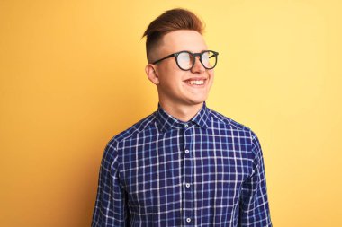 Sarı arka planda gözlüklü, sıradan tişörtlü yakışıklı bir adam yüzünde gülümseme, doğal bir ifade ile yan yana bakıyor. Kendinden emin gülen.