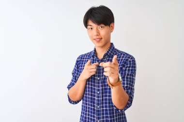 Sıradan mavi gömlekli genç adam izole edilmiş beyaz arka planda durmuş mutlu ve komik yüzlü parmakları kameraya doğrultuyor. İyi enerji ve titreşimler.