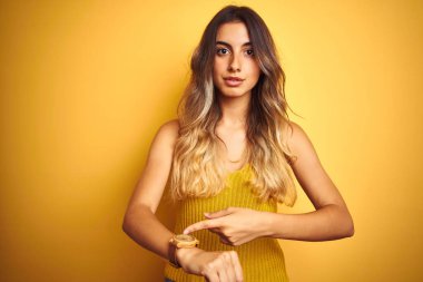 Sarı arka planda tişört giyen güzel bir kadın. Aceleyle saati, sabırsızlığı ve gecikmeye kızmayı işaret ediyor.