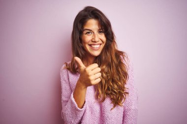 Pembe soyutlanmış arka planda duran süveter giyen genç ve güzel bir kadın elleriyle mutlu bir jest yapıyor. Kameraya bakıp başarıyı gösteren ifade onaylanıyor.