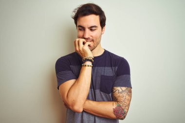 İzole edilmiş beyaz arka plan üzerine gündelik tişört giyen genç ve yakışıklı bir adam elleri ağız yiyen tırnaklarla stresli ve gergin görünüyor. Endişe sorunu.