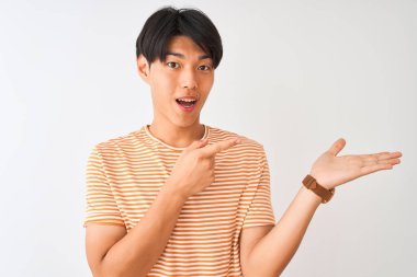 Sıradan çizgili tişört giyen genç Çinli bir adam izole edilmiş beyaz arka planda durup kameraya hayret ediyor ve gülümsüyor..