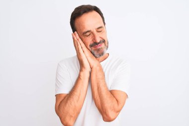 Orta yaşlı yakışıklı bir adam, günlük tişört giyip izole edilmiş beyaz arka planda dikiliyor. Yorgun uyuyor, hayal kuruyor ve elleri ile birlikte poz veriyor, gözleri kapalı gülümsüyor..