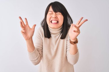 Genç, güzel, balıkçı yaka kazak giyen Çinli bir kadın izole edilmiş beyaz arka plan üzerine çılgın ve başarıyı kutluyor kollarını kaldırmış ve gözlerini kapatmış heyecanlı çığlıklar atıyor. Kazanan konsept