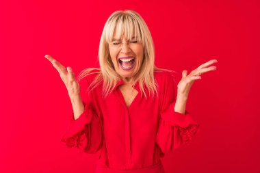 Soyutlanmış kırmızı arka planda duran zarif bir gömlek giyen orta yaşlı kadın, başarı için deli ve çılgınlığını kollarını kaldırarak ve gözlerini kapatarak heyecanla haykırarak kutluyor. Kazanan konsept