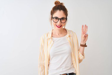 Kızıl saçlı kadın çizgili gömlek ve gözlük takıyor. İzole edilmiş beyaz arka plan üzerinde duruyor. Üç numaralı parmaklarıyla işaret ediyor..