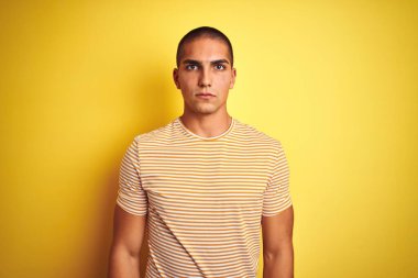 Sarı yalıtılmış arka plan üzerine çizgili tişört giyen yakışıklı bir genç. Yüzünde ciddi bir ifade var. Basit ve doğal bir şekilde kameraya bakıyorsun..