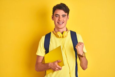 Kulaklık ve sırt çantası takan genç bir çocuk izole edilmiş arka planda kitap okuyor. Gururla bağırıyor, zaferi kutluyor ve başarıyı kutluyor. Çok heyecanlı, coşkulu bir duygu.