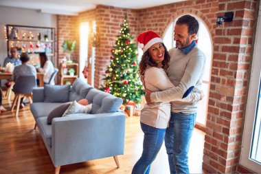 Aile ve arkadaşlar Noel arifesini geleneksel yemek ve dekorasyonla evde kutluyorlar. Romantik son sınıf çifti birbirine sarılıyor.