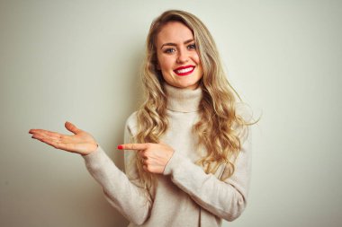 İzole edilmiş beyaz arka planda balıkçı yaka kazak giyen güzel bir kadın kameraya hayret ediyor ve gülümsüyor..