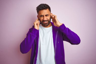 Mor eşofman üstü giyen genç bir Hintli yüksek sesli müzik sesi için pembe arka planda dikiliyor kulakları parmaklarıyla kapatıyor. Sağır kavramı.