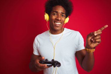 Oyun oynayan Afro-Oyuncu, izole edilmiş kırmızı arkaplan üzerinde joystick kulaklıklar kullanarak el ve parmak ile mutlu bir şekilde oyun oynuyor.