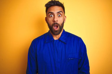 Sarı arka plan üzerinde üniforma giyen yakışıklı Hintli işçi korku, korku ve heyecan dolu bir yüz ifadesinden korkuyor ve şoka uğruyor..