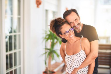 Orta yaşlı, güzel bir çift terasta durup sarılıyor ve gülümsüyor.