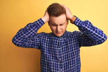 Genç yakışıklı adam rahat gömlek giyen izole sarı arka plan üzerinde baş ağrısı umutsuz acı ve stresli çünkü ağrı ve migren. Eller baş üstünde.