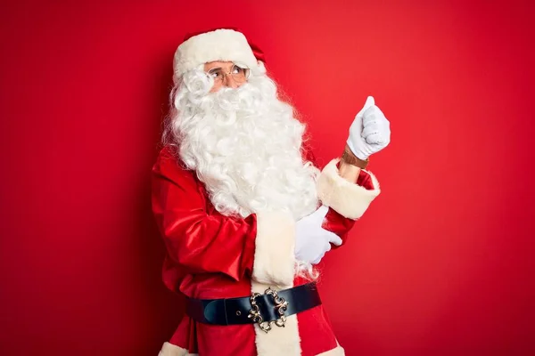 中年男子 穿着圣诞老人的服装 站在孤立的红色背景上看起来很自豪 微笑着向旁边竖起大拇指 — 图库照片