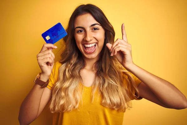 Młoda Piękna Kobieta Trzymająca Kartę Kredytową Żółtym Tle Zaskoczona Pomysłem — Zdjęcie stockowe