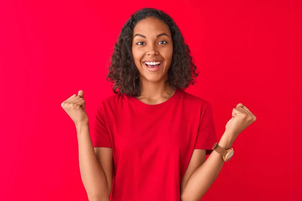穿着T恤衫站在孤立的红色背景之上的年轻的巴西女人自豪地尖叫着 庆祝胜利和成功 非常兴奋 欢呼着感情 — 图库照片