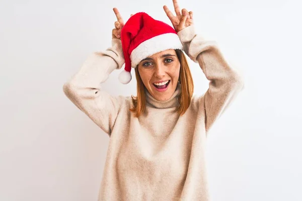 美しい赤毛女性身に着けているクリスマスの帽子上の隔離された背景面白いとクレイジーなポーズ指で頭の上にウサギの耳として 笑顔陽気に — ストック写真
