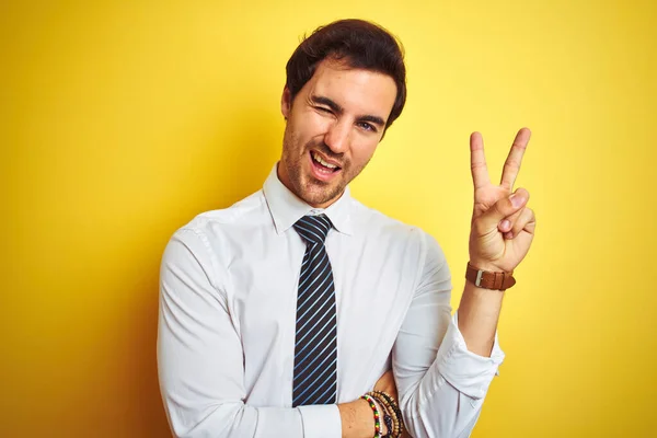 優雅なシャツを着た若いハンサムなビジネスマンは 勝利のサインを行うカメラで幸せな顔のウィンクで笑顔孤立した黄色の背景にネクタイ 第二番 — ストック写真