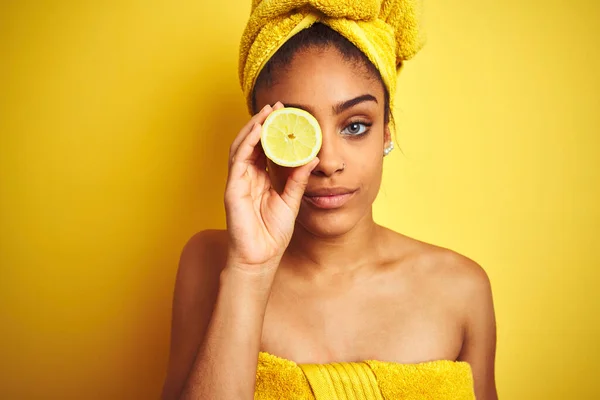 シャワー後にタオルを身に着けているアフロ女性は深刻な考え方スマート顔に自信を持って式で隔離された黄色の背景にスライスレモンを保持 — ストック写真