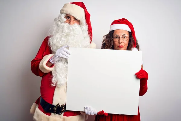 上了年纪的夫妇穿着圣诞老人的服装 拿着横幅挂在孤立的白色背景上 脸上带着自信的表情 严肃地思考着 — 图库照片