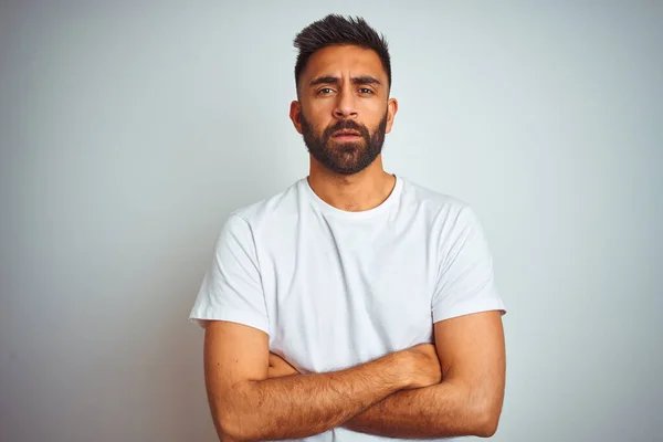 Young indian man wearing t-shirt standing over isolated white background skeptic and nervous, disapproving expression on face with crossed arms. Negative person.