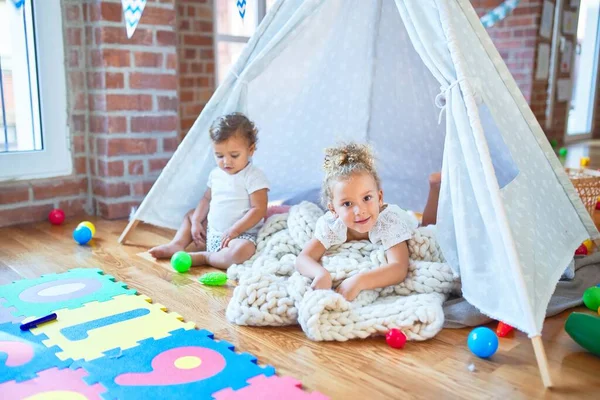 Beautiful toddlers playing inside tipi over blanket around lots of toys at kindergarten