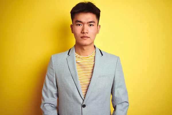顔に深刻な表現と隔離された黄色の背景に立ってジャケットを身に着けている若いアジアの中国のビジネスマン シンプルで自然なカメラを見て — ストック写真